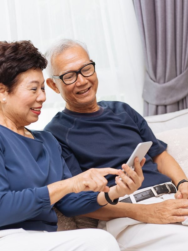 Senior Asian couple grandparents using a smart phone together on sofa at home