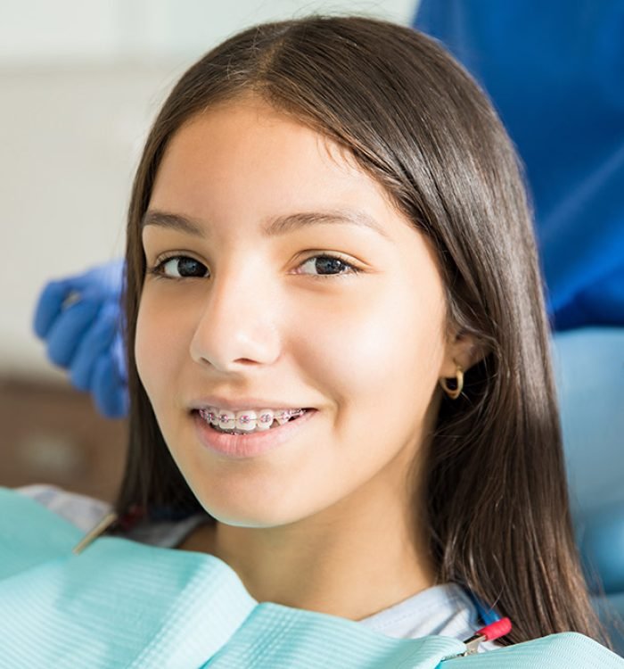 Close-up portrait of smiling teenage girl with braces against dentist standing in clinic