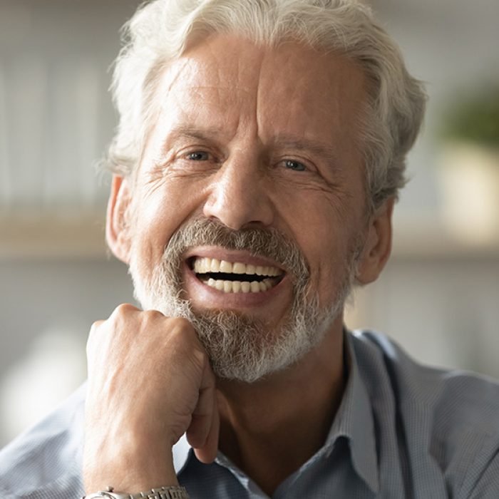 Close up portrait handsome face of 60s elderly man having candid wide toothy smile put fist under chin looking at camera concept of healthy person enjoy retired life, dentures services for old people