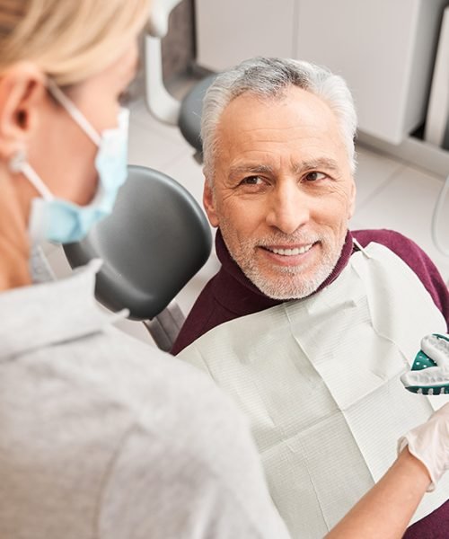 New smile. Back view of the female blonde caucasian doctor presenting dental impression for dentures to the senior smiling man. Stock photo